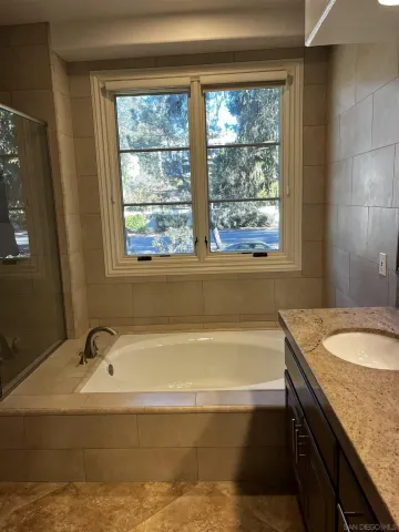 a bathroom with a granite countertop tub a sink and a window