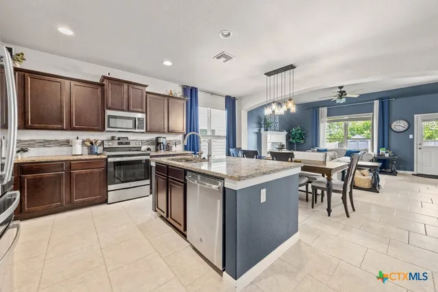 a kitchen with stainless steel appliances granite countertop a stove top oven a sink a dining table and chairs