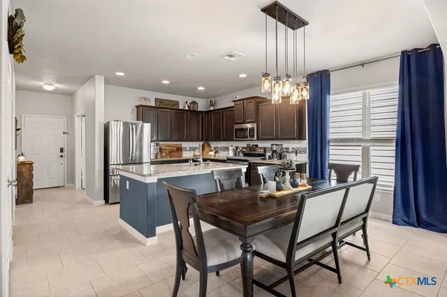 a kitchen with kitchen island a dining table chairs stainless steel appliances and cabinets