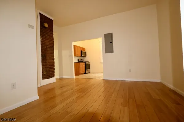 a view of empty room with wooden floor and kitchen