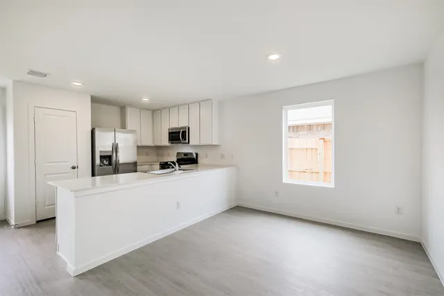 a large white kitchen with stainless steel appliances granite countertop a stove a sink a refrigerator and white cabinets with wooden floor