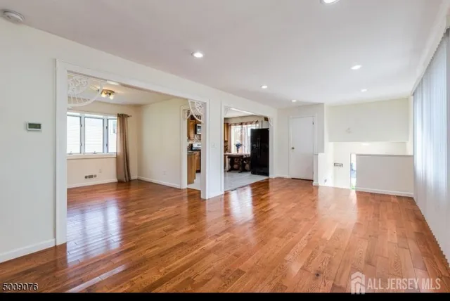 a view of an empty room with wooden floor and kitchen space