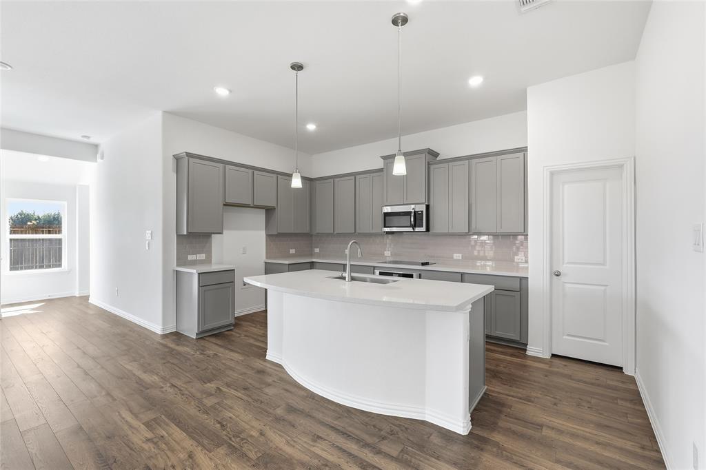 2529 Rivers W Road Anna, TX 75409 - Photo 11 of 40 Kitchen featuring an expansive island with a built-in sink, stainless steel appliances, gray shaker-style cabinetry, and wood-finish flooring