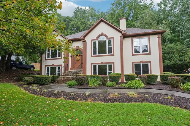 a view of a yard in front of a house with plants and large trees