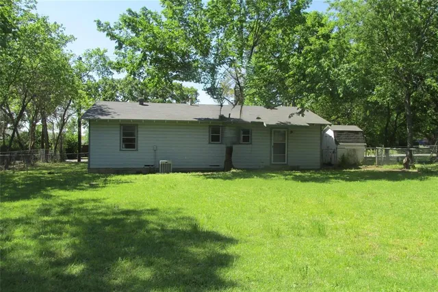 a backyard of a house with plants and a large tree
