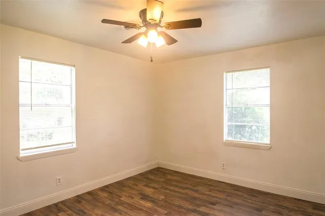 an empty room with wooden floor ceiling fan and windows