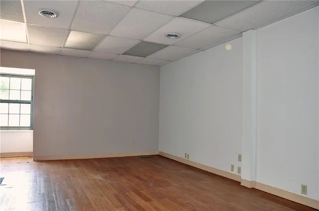 an empty room with wooden floor and windows with curtains
