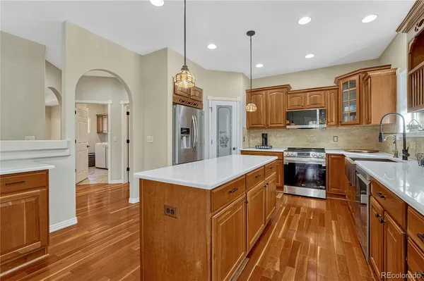 a kitchen with stainless steel appliances granite countertop a stove top oven a sink dishwasher a refrigerator and a dining table with wooden floor