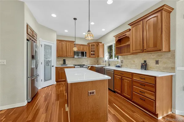 a kitchen with stainless steel appliances granite countertop a refrigerator a sink dishwasher a stove and white countertops with wooden floor