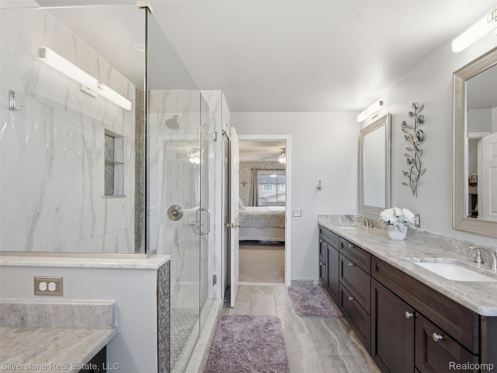 6577 Edith Court Troy, MI 48085 - Photo 37 of 61 Bathroom featuring dual dark wood vanities with integrated sinks and light-toned countertops, a glass-enclosed shower with subway tile surround, and large format floor tiling