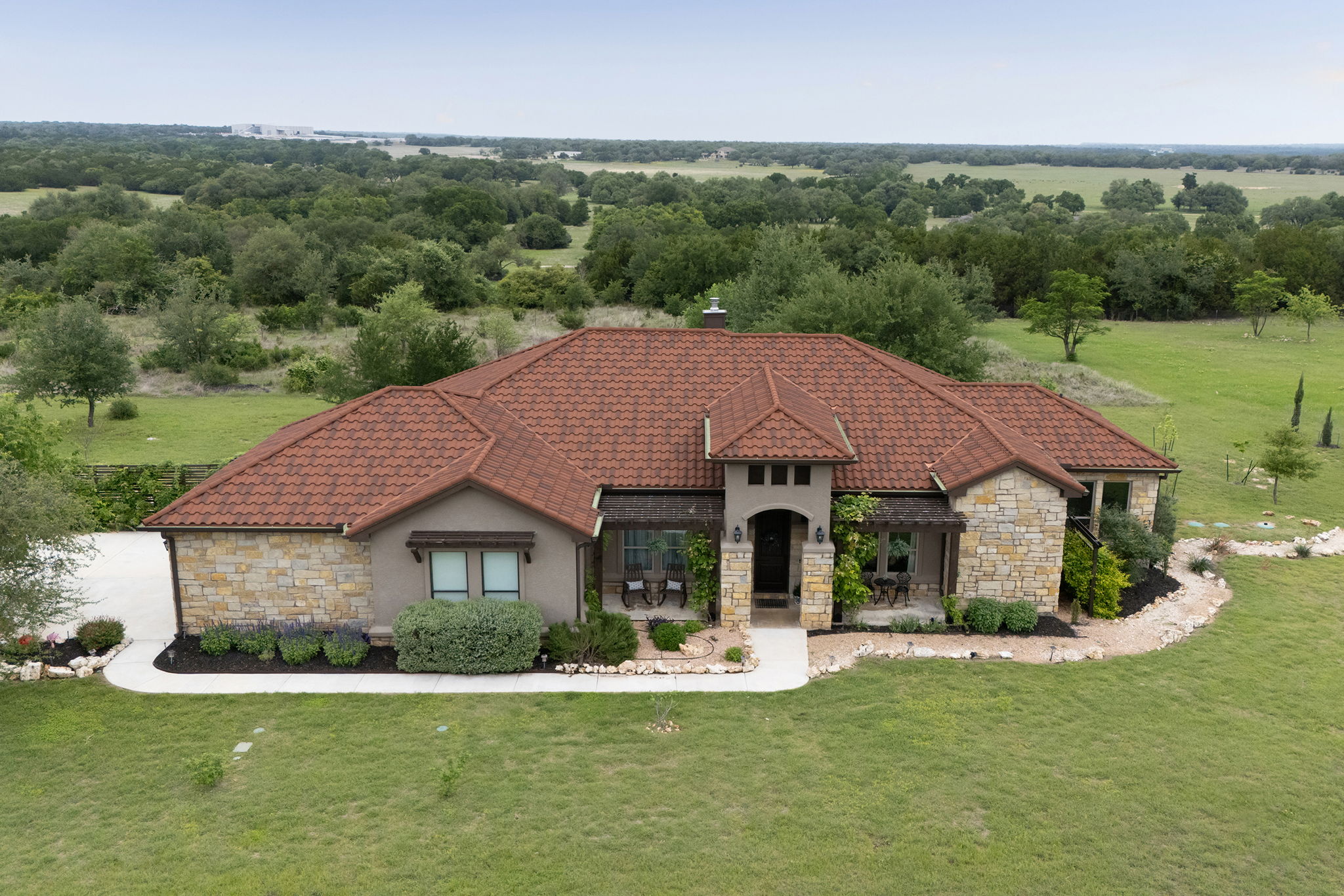 Elegant single-story home with stone and stucco exterior, tile roof, and a welcoming covered front entry, set on a spacious lot with scenic countryside views.