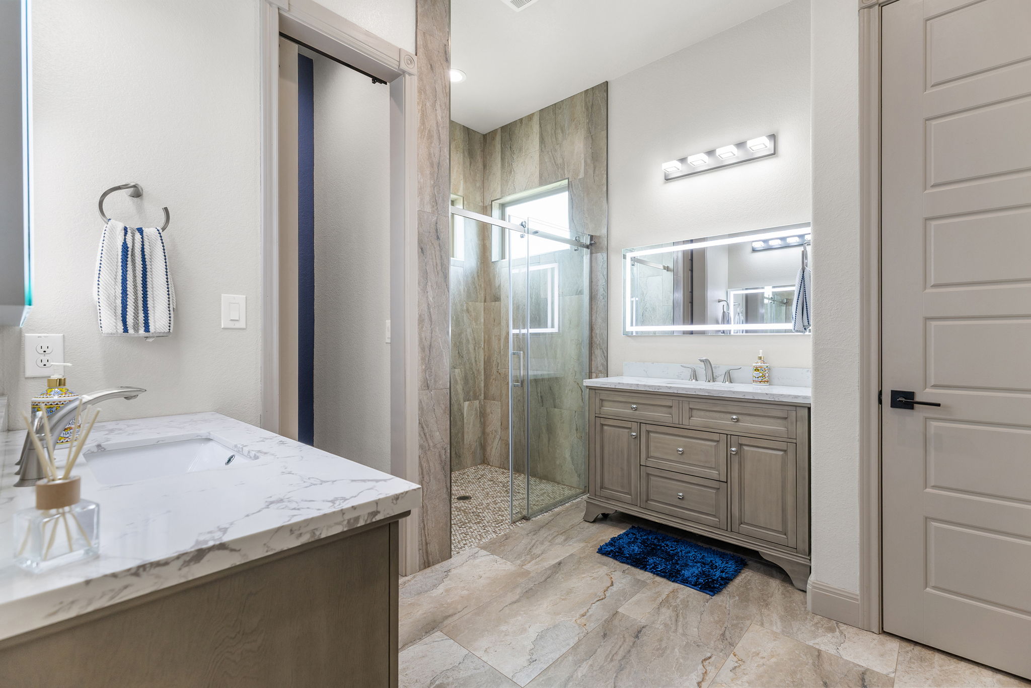 128 Strada Luca Florence, TX 76527 - Photo 18 of 40 Contemporary bathroom with dual vanities, marble-look countertops, walk-in glass shower with pebble floor, and large-format tile flooring.