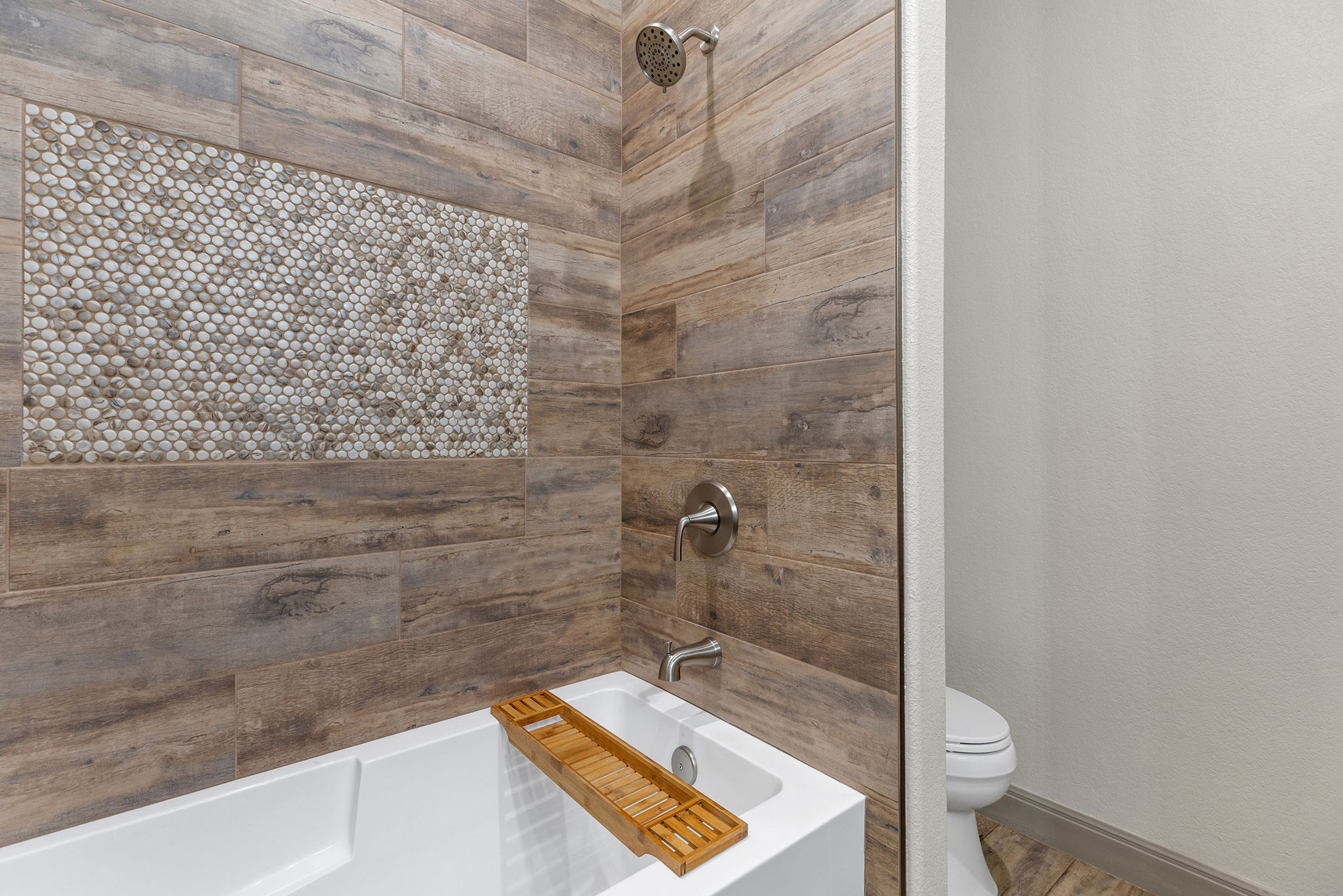 128 Strada Luca Florence, TX 76527 - Photo 25 of 40 Tub and shower combo with wood-look tile surround, pebble accent band, and modern fixtures.