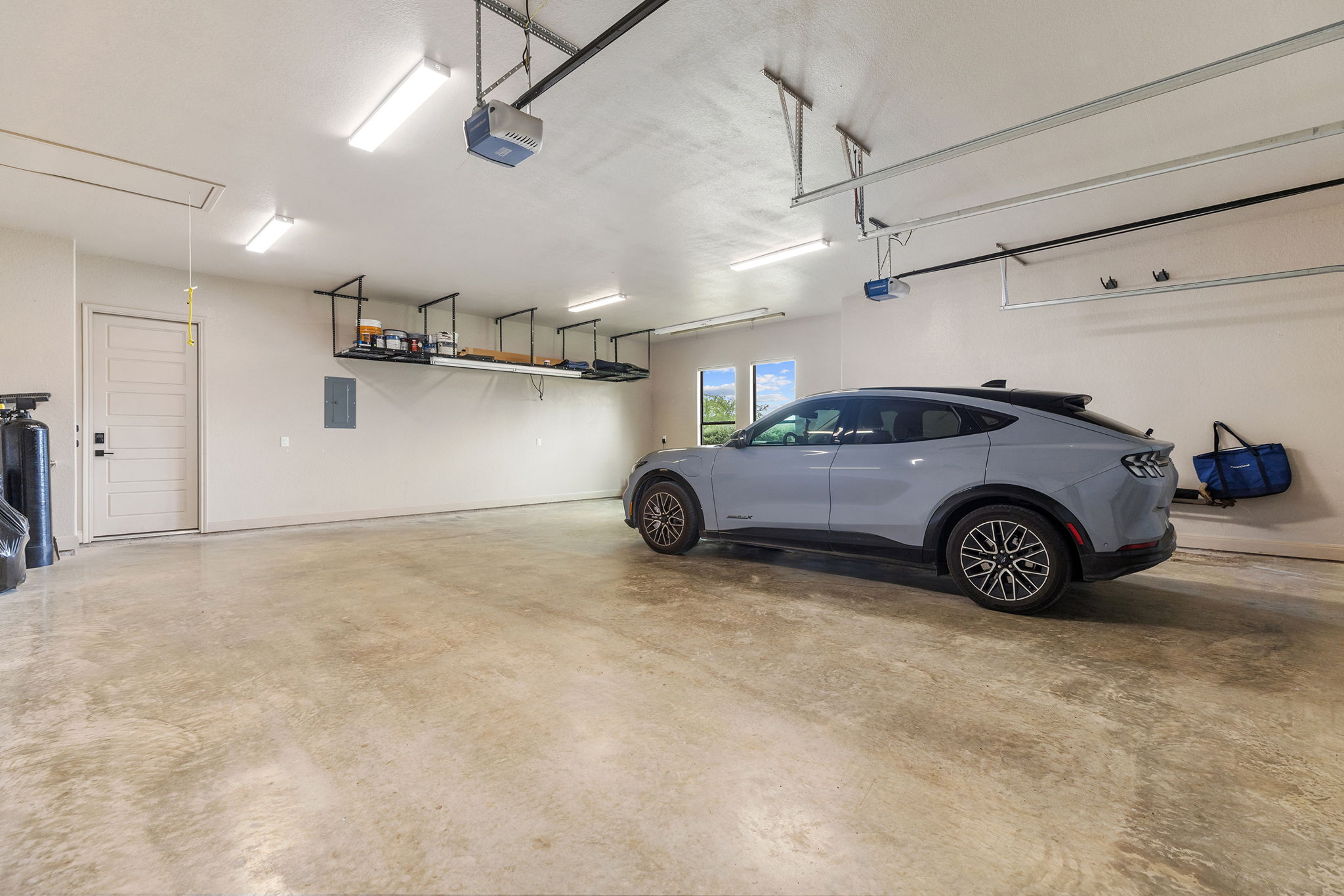 128 Strada Luca Florence, TX 76527 - Photo 30 of 40 Expansive garage with durable concrete flooring, overhead storage racks for added organization, dual garage door openers, and natural light from two windows, plus a convenient side access door for easy entry.