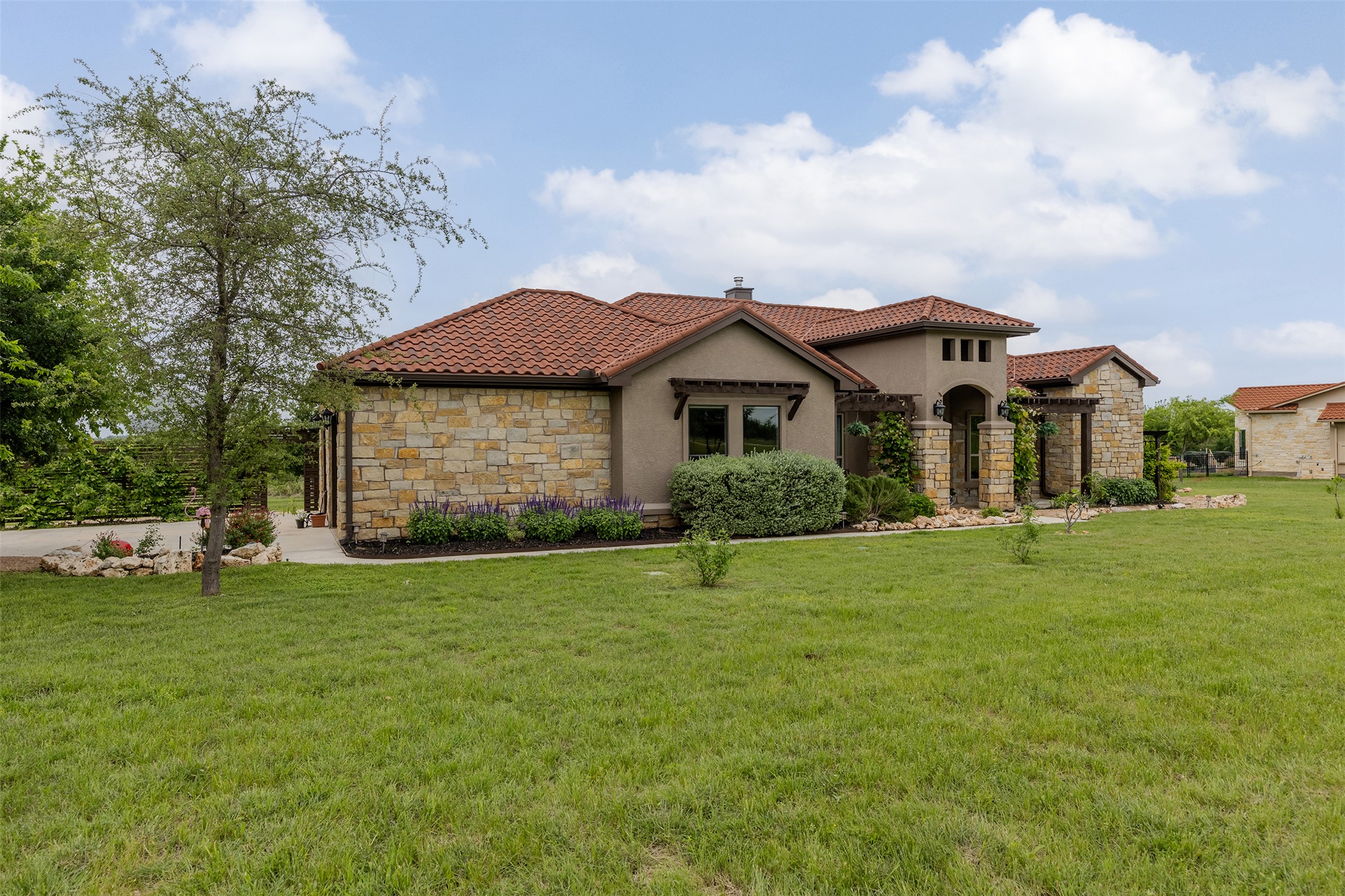 128 Strada Luca Florence, TX 76527 - Photo 3 of 40 Mediterranean-style exterior with red tile roof, stucco and stone accents, landscaped beds, and a welcoming covered entry framed by mature greenery.