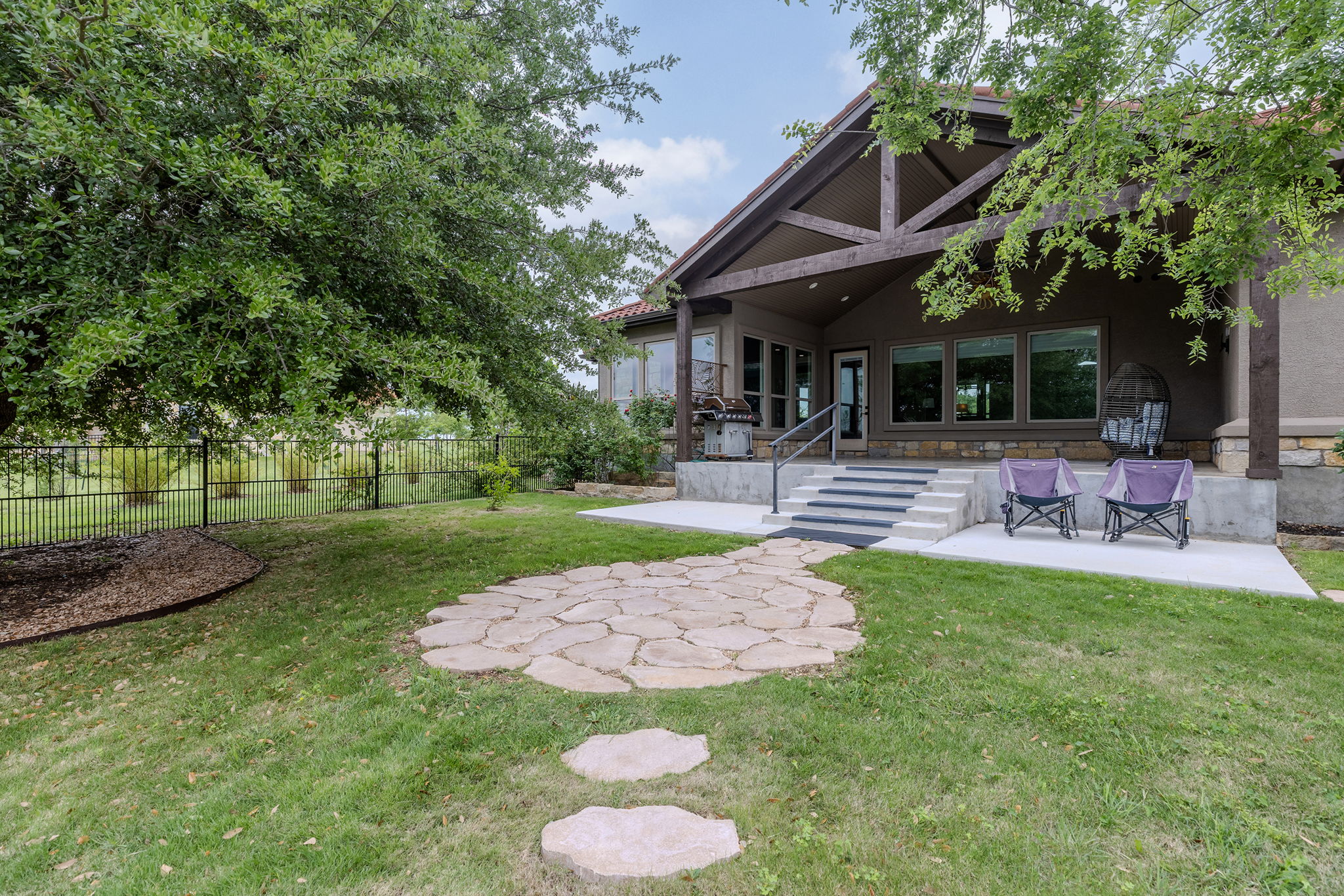 128 Strada Luca Florence, TX 76527 - Photo 31 of 40 Expansive backyard retreat featuring a covered patio with exposed wood beams, a spacious concrete entertaining area, and a charming flagstone pathway, all surrounded by mature trees and a fully fenced yard for added privacy.