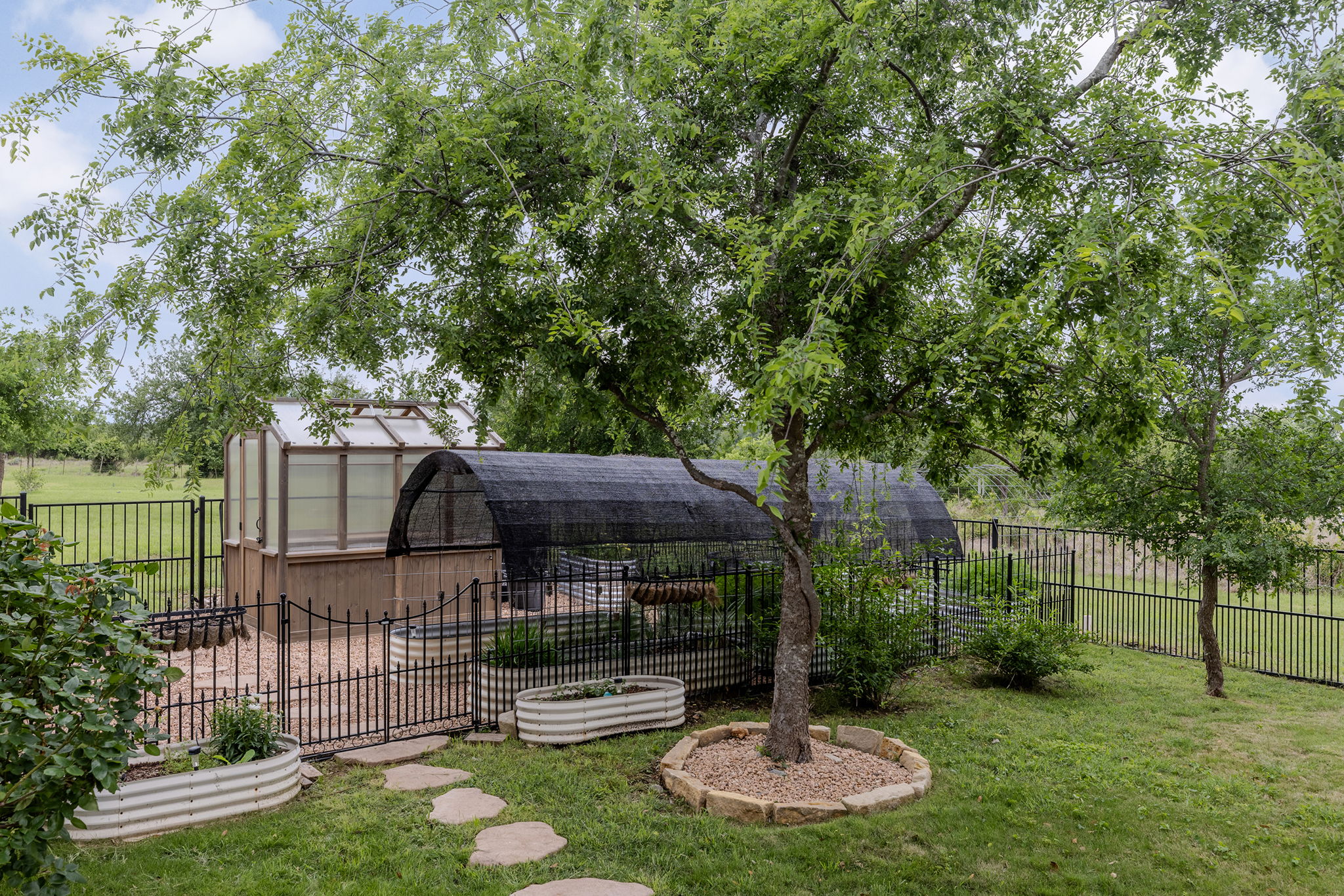 128 Strada Luca Florence, TX 76527 - Photo 33 of 40 Well-appointed garden retreat featuring a greenhouse, an additional covered growing structure, and multiple raised planting beds, all enclosed within a fenced area and surrounded by mature trees for a private, functional outdoor space.