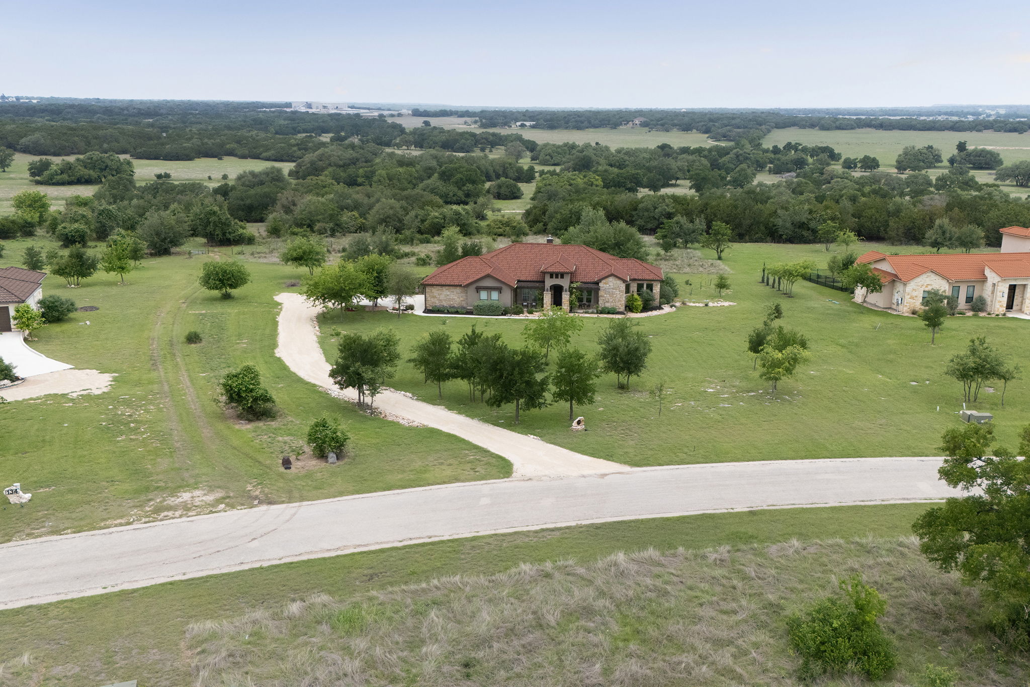128 Strada Luca Florence, TX 76527 - Photo 36 of 40 Single-story residence showcasing a timeless stone façade and terracotta-tiled roof, set on a spacious homesite with a long curved driveway, mature trees, and sweeping countryside views.