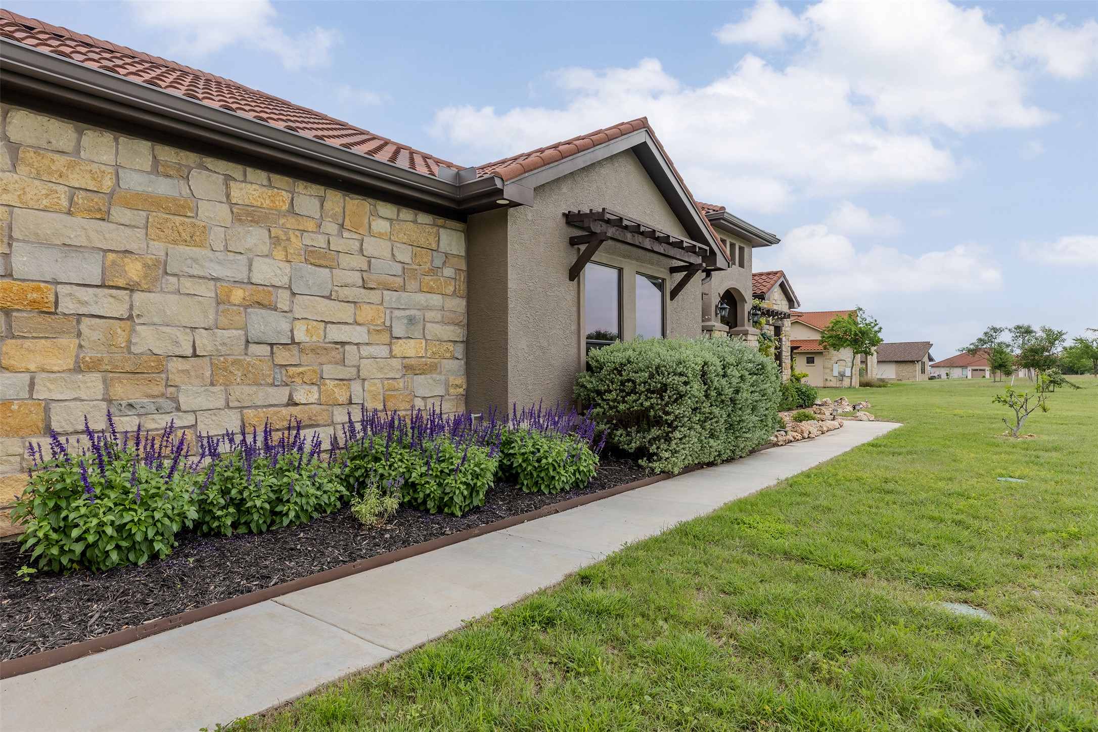 128 Strada Luca Florence, TX 76527 - Photo 5 of 40 Exterior featuring stone and stucco finishes with a red tile roof, highlighted by landscaped beds and a walkway along the home.