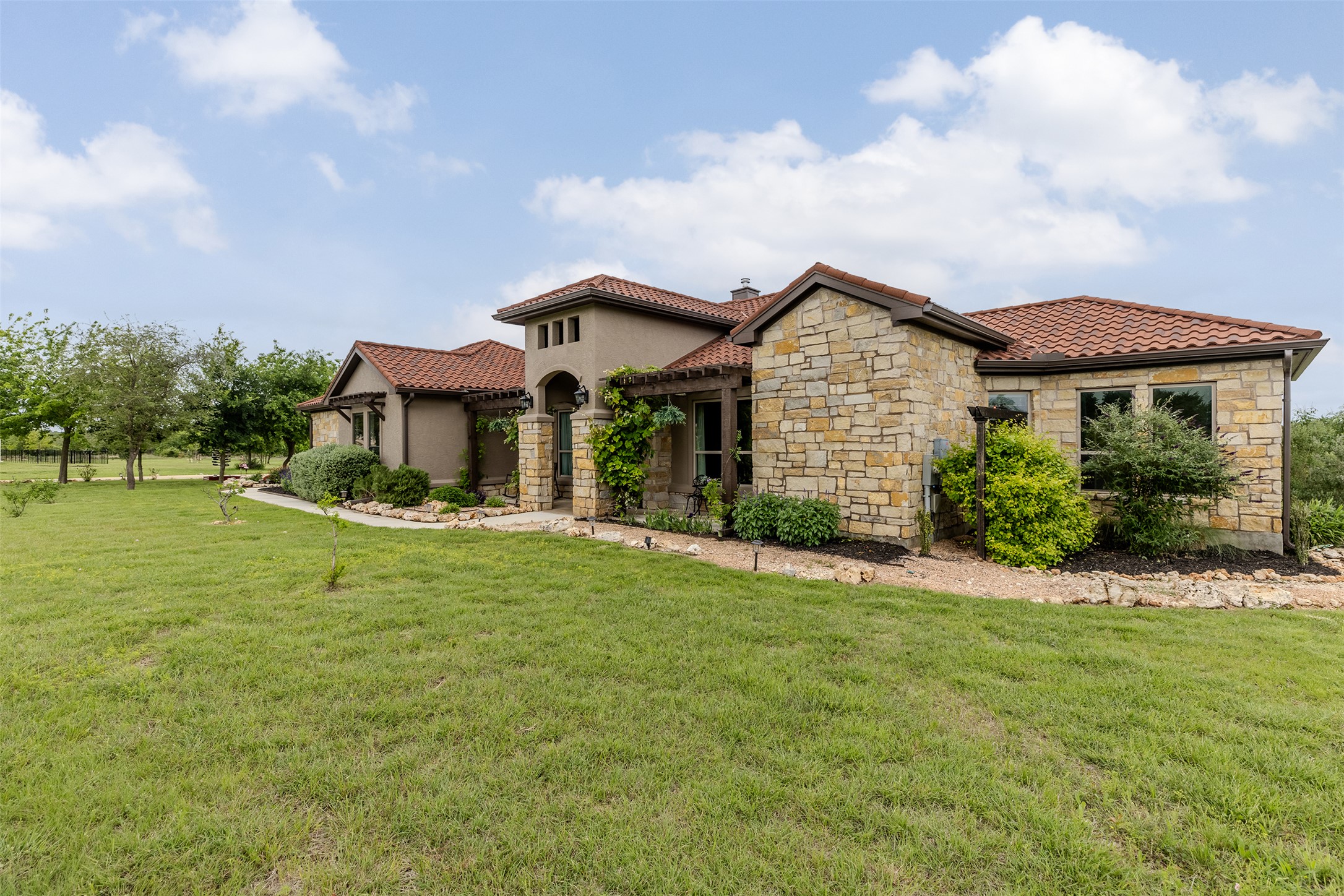 128 Strada Luca Florence, TX 76527 - Photo 6 of 40 Mediterranean-style exterior with red tile roof, stone and stucco finishes, arched entry, and landscaped yard with open green space.
