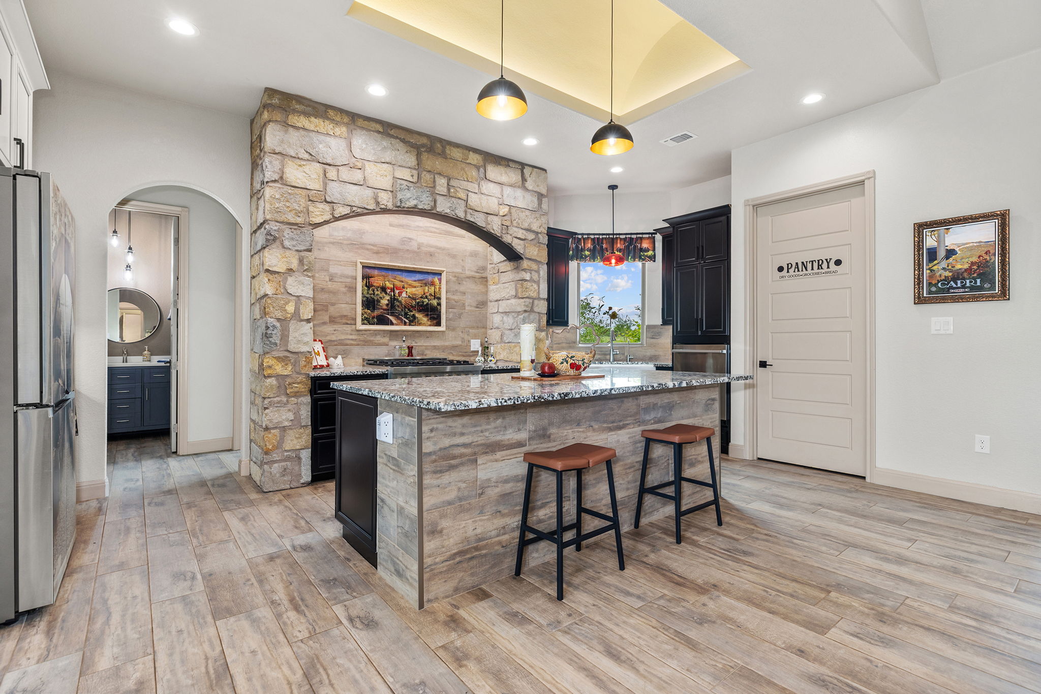 128 Strada Luca Florence, TX 76527 - Photo 8 of 40 Spacious kitchen with a large granite island, stone-clad archway, wood-look flooring, and pantry access for added convenience.