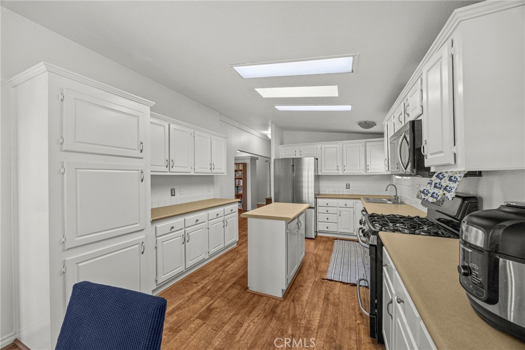 23301 Ridge Rte Drive, Unit 229 Laguna Hills, CA 92653 - Photo 6 of 28 a kitchen with a refrigerator a stove and white cabinets with wooden floor
