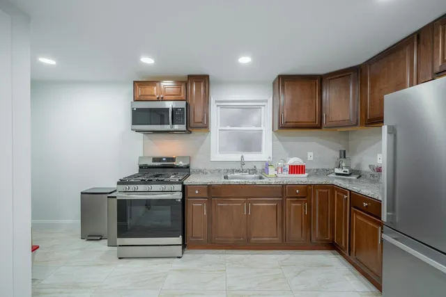 a kitchen with stainless steel appliances granite countertop a stove top oven a sink dishwasher and a refrigerator with wooden cabinets