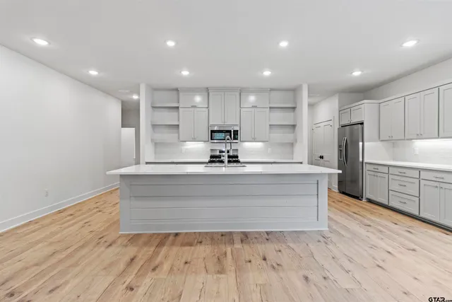a view of kitchen center island wooden floors stainless steel appliances and cabinets