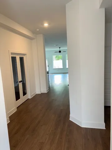 a view of a hallway to an empty room with wooden floor and windows