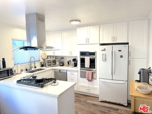a kitchen with a refrigerator a stove a sink and white cabinets with wooden floor