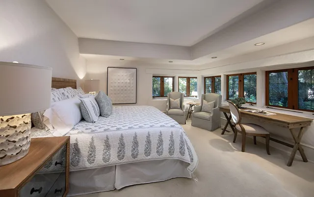 a bedroom with a bed a table and large windows