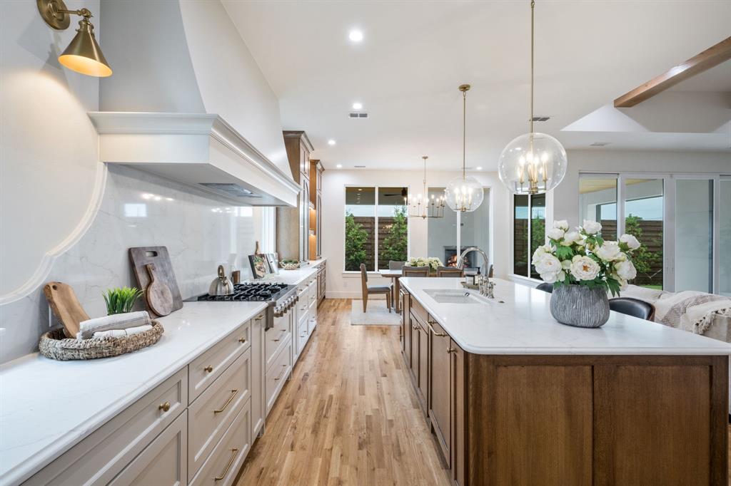 3304 Ferguson Road Grapevine, TX 76092 - Photo 19 of 38 Spacious kitchen featuring an extended island with integrated sink, wood-finish flooring, a built-in range with an ornate hood, and pendant lighting