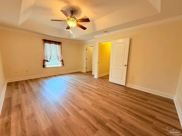 a view of an empty room with wooden floor and a ceiling fan
