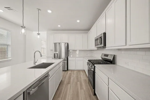 a kitchen with stainless steel appliances granite countertop a sink a stove top oven and wooden floor