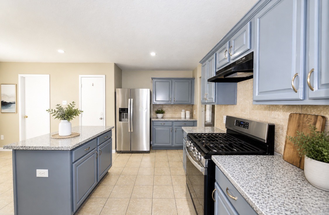 9611 Babbling Spring Court Tomball, TX 77375 - Photo 13 of 31 Modern kitchen with light blue cabinets, granite countertops, and stainless steel appliances. Features a spacious island and beige tile flooring, offering a bright and functional space.