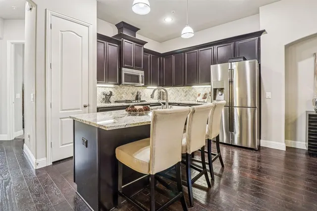 a kitchen with stainless steel appliances granite countertop a dining table chairs refrigerator and sink