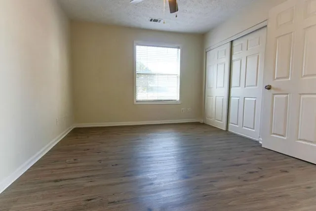 an empty room with wooden floor chandelier fan and windows