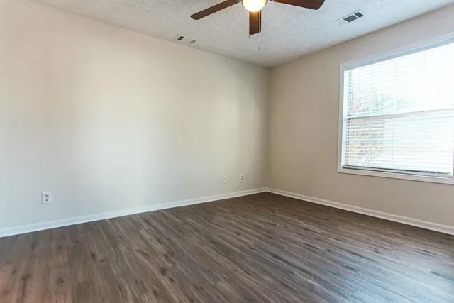 an empty room with wooden floor a ceiling fan and kitchen view