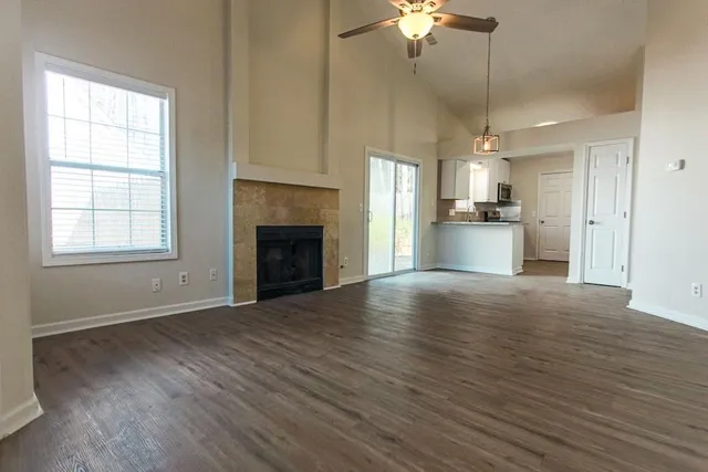 an empty room with wooden floor a fireplace a ceiling fan and windows