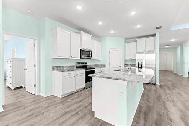 a large kitchen with stainless steel appliances granite countertop a refrigerator a sink a stove and white cabinets with wooden floor