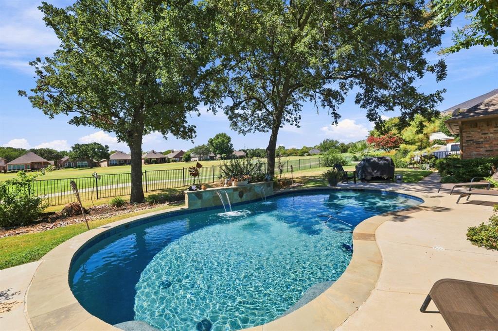 1762 Timber Ridge Circle Corinth, TX 76210 - Photo 28 of 29 Freeform swimming pool with stone coping, integrated water features, expansive patio, and mature trees