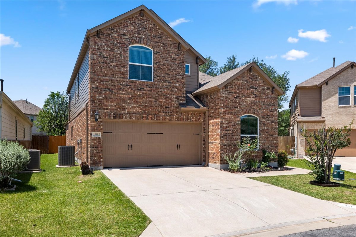 3451 Mayfield Ranch Boulevard, Unit 311 Round Rock, TX 78681 - Photo 3 of 40 Brick and siding exterior featuring an arched window, a two-car garage, concrete driveway, and established landscaping