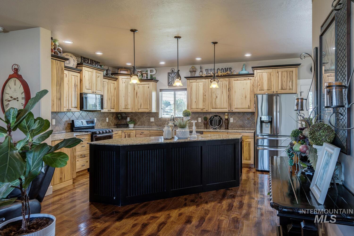 22757 Rosicky Way Caldwell, ID 83607 - Photo 12 of 50 Kitchen with a center island, appliances with stainless steel finishes, decorative light fixtures, dark wood-style floors, and backsplash