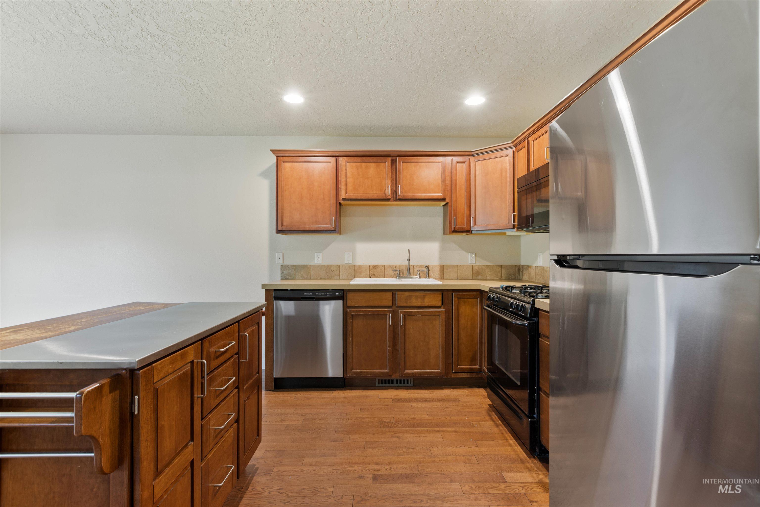 2209 South Amy Avenue Boise, ID 83706 - Photo 12 of 30 Kitchen with black appliances, light countertops, recessed lighting, light wood-type flooring, and brown cabinetry