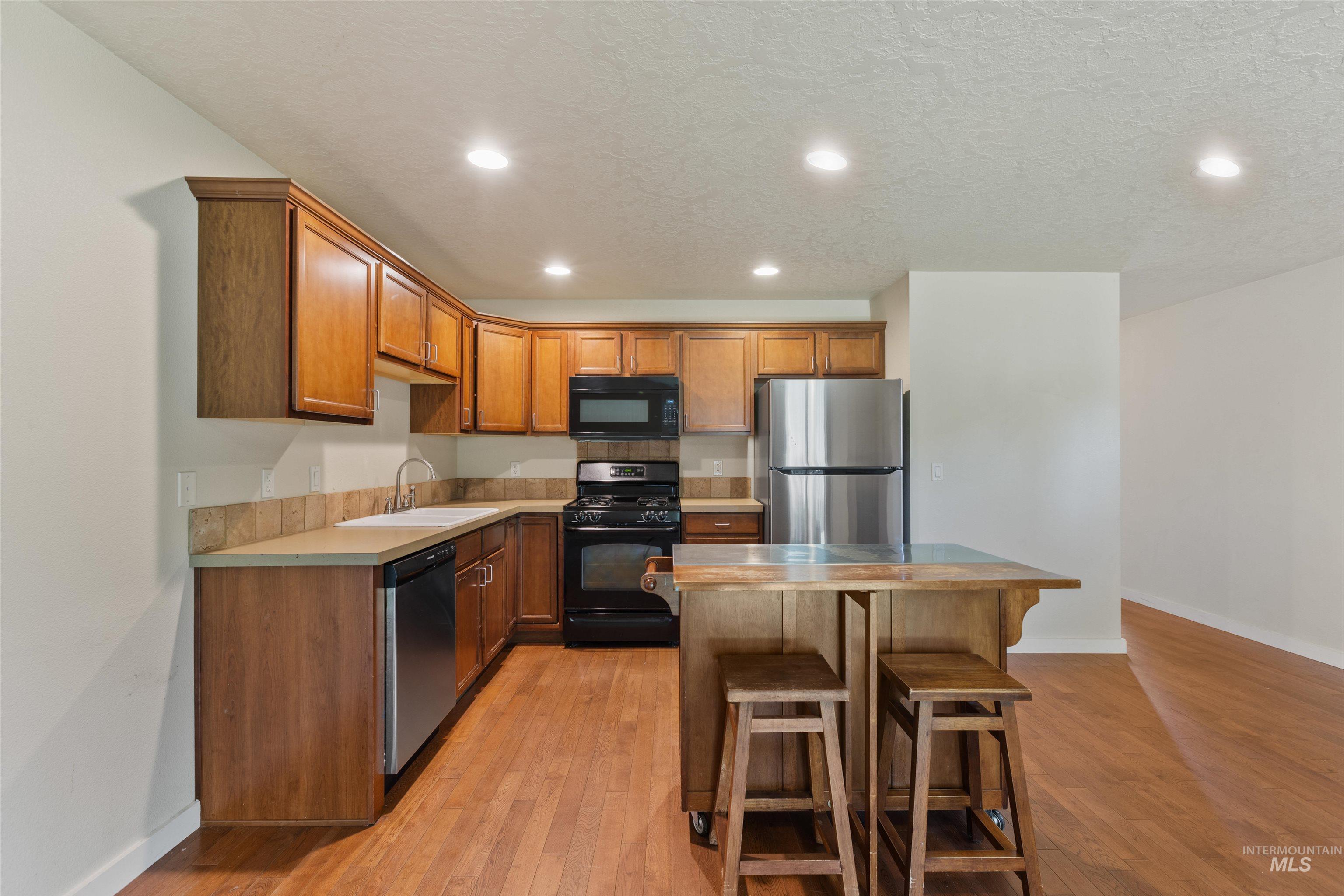2209 South Amy Avenue Boise, ID 83706 - Photo 14 of 30 Kitchen featuring recessed lighting, black appliances, brown cabinetry, a breakfast bar area, and light countertops
