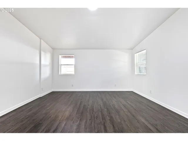 a view of an empty room with wooden floor and window