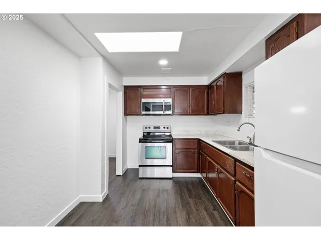 a kitchen with granite countertop a refrigerator stove a sink and dishwasher with wooden floor