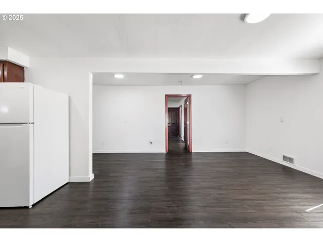a view of an empty room with wooden floor and a refrigerator