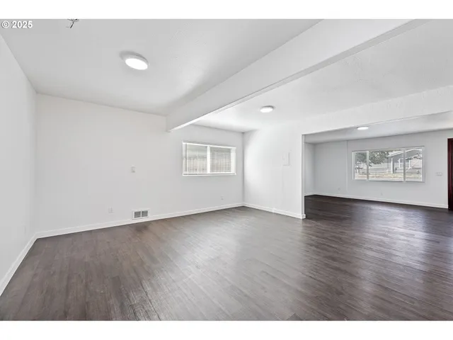 a view of an empty room with a window and wooden floor