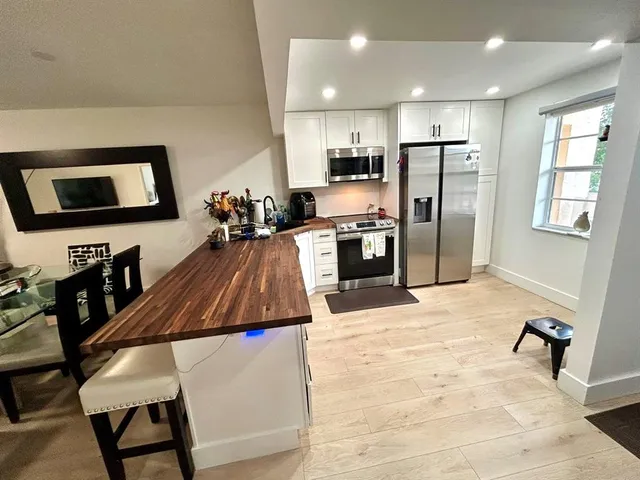 a kitchen with stainless steel appliances kitchen island granite countertop a refrigerator a stove top oven a sink dishwasher and dining table with wooden floor